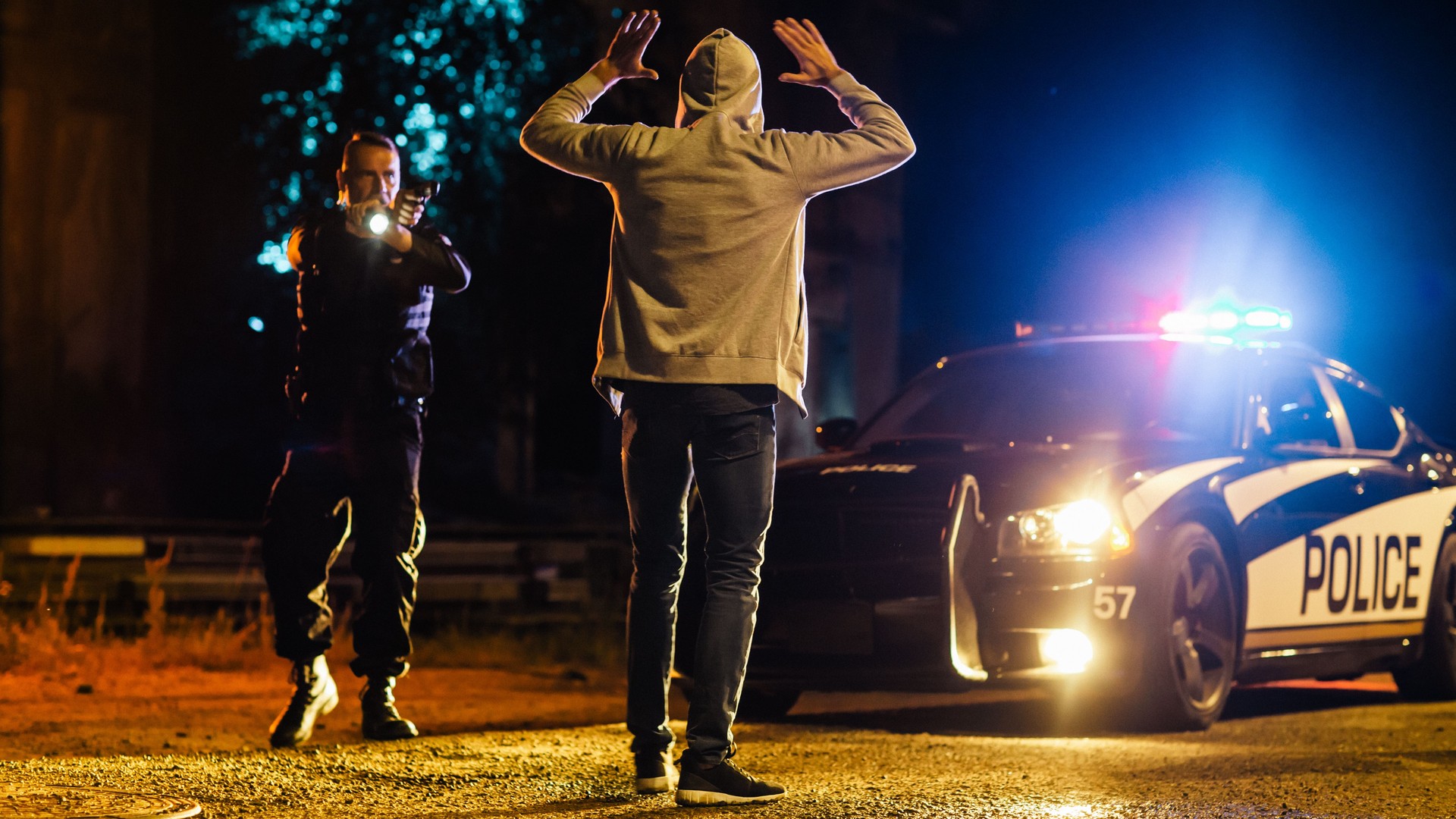 Middle Aged Caucasian Police Officer Aims at a Suspect. Police Using a Weapon to Intimidate Wanted Criminal. Suspect Raising his Hands in Compliance. Police Successfully Making an Arrest